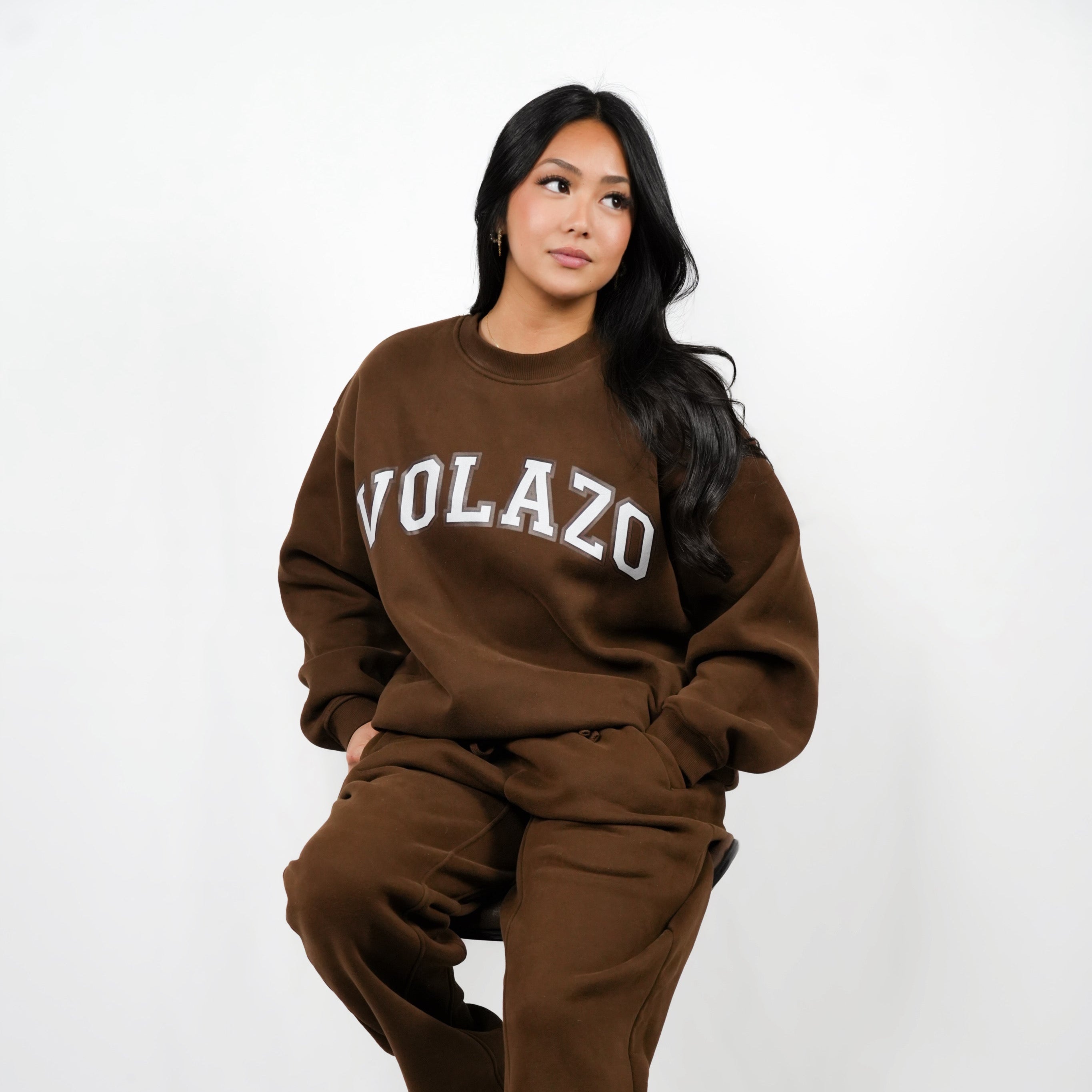 Person wearing a brown 'VOLAZO' sweatshirt and pants on a white background
