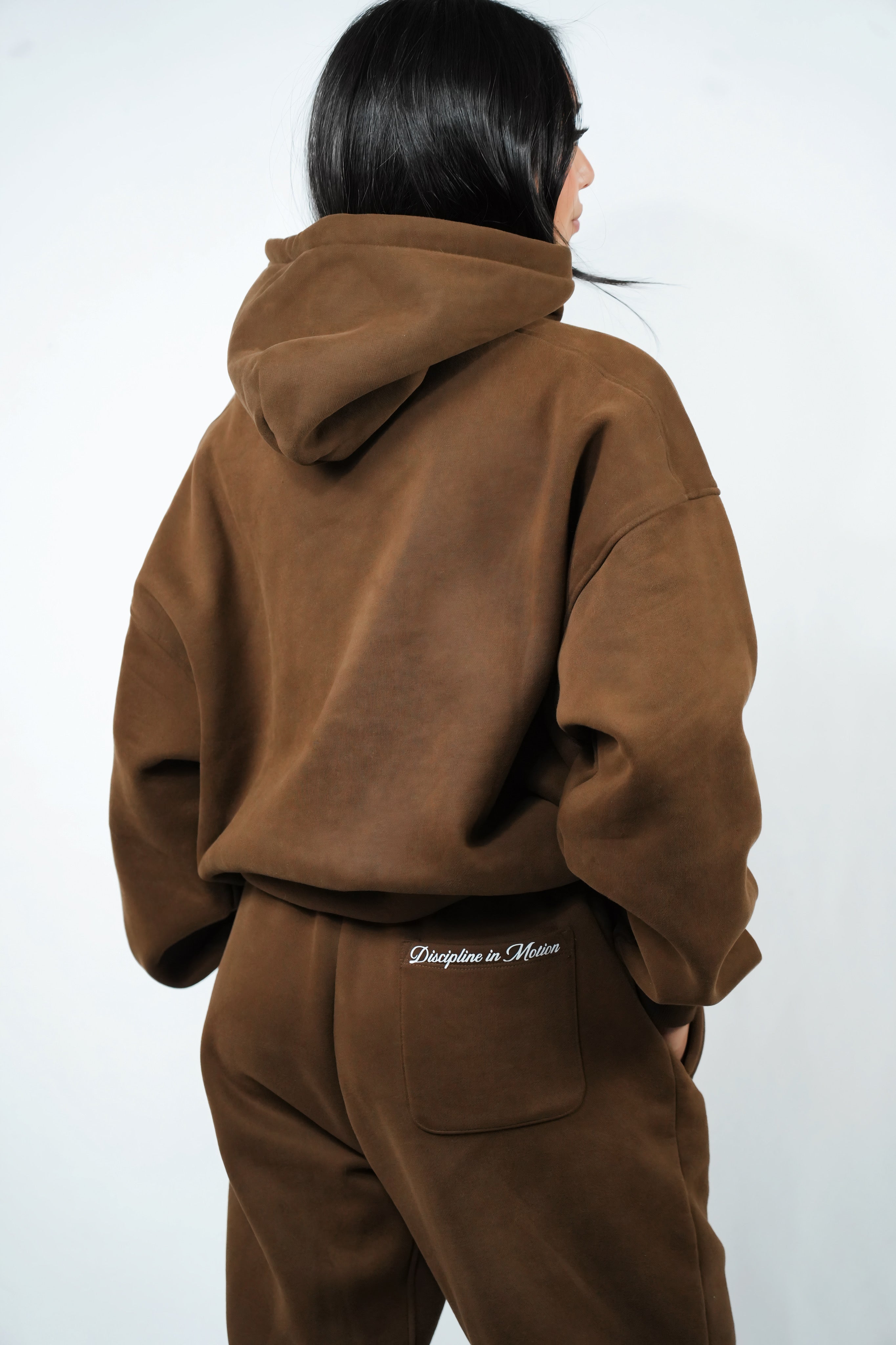 Person wearing a brown tracksuit with 'Discipline in Motion' branding on a white background