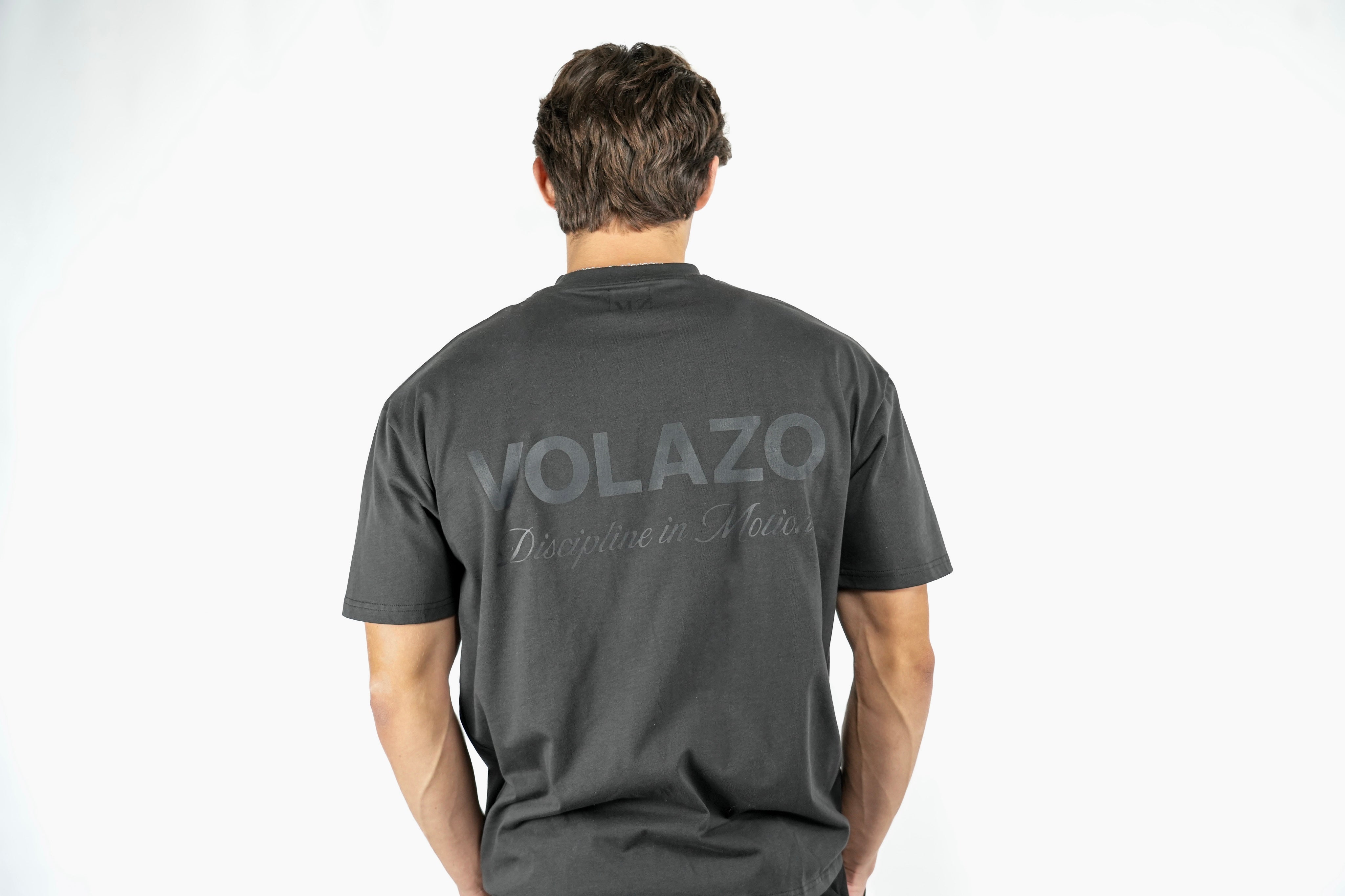 Person wearing a charcoal t-shirt with 'VOLAZON' branding on the back against a white background